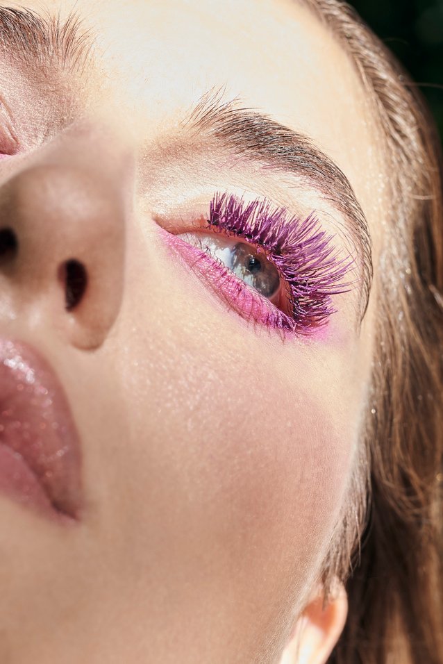 Makeup by Lucia Pilin on caucasian model. Purple false lashes paired with a pink liner to create a colorful editorial look, paired with contoured glossy lips.